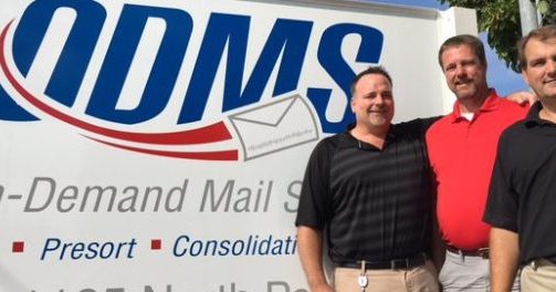 Tim Ticckles, Mike Ticckles, and Rob Quick of On Demand Mail Services pose for a group photo in front of an O.D.M.S. sign outside