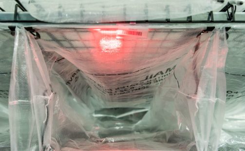 A U.S.P.S. mail bag attached to Engineering Innovation's LightSort Sort-to-Light bag rack is lit up with a red L.E.D.