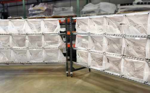 The LightSort Bag Rack with Sort-to-Light and attached U.S.P.S. Mail bags attached sits in a warehouse with a blurry background