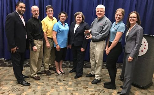 Engineering Innovation C.O.O. Don Caddy accepting the 2017 USPS Award from the Post Master General while standing next to several other Engineering Innovation employees