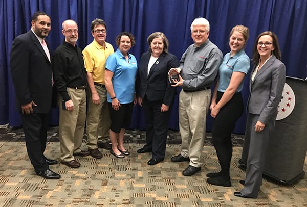 Engineering Innovation C.O.O. Don Caddy accepting the 2017 USPS Award from the Post Master General while standing next to several other Engineering Innovation employees