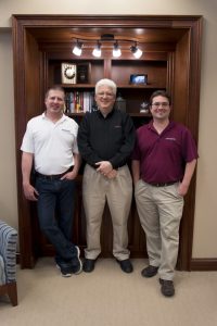 Don Caddy, Adam Fleming, and Aaron Pedigo, the founders of Engineering Innovation, pose for a group photo in front of a bookcase in the new Engineering Innovation office