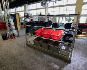 The Carton Flow Rack solution with light-directed technology sits on gray carpet in Engineering Innovation's racecar themed trade show booth at Parcel Forum 2021