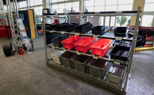 The Carton Flow Rack solution with light-directed technology sits on gray carpet in Engineering Innovation's racecar themed trade show booth at Parcel Forum 2021