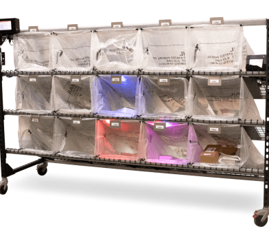 A large parcel sorting system with transparent bags is filled with various packages and letters. Each bag is labeled with destinations, some illuminated by colored lights. The entire system is mounted on wheels for mobility.