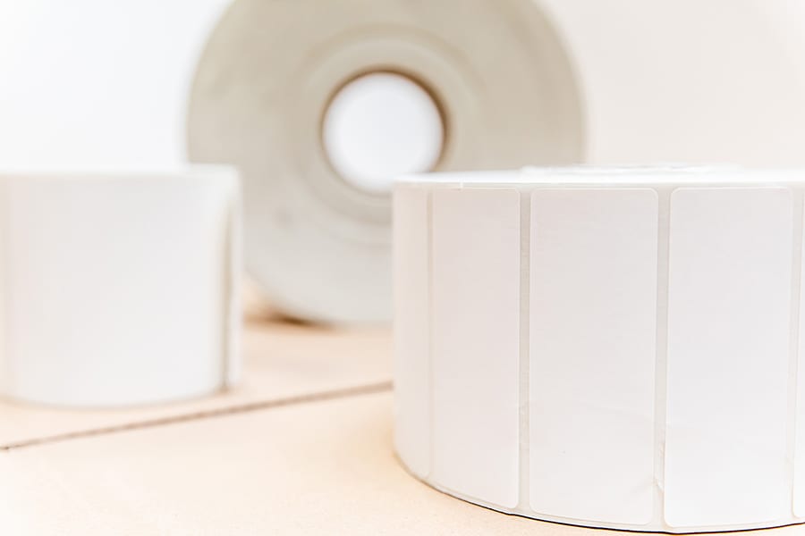 Close-up image of several rolls of blank adhesive labels. The labels are white and arranged in rolls on a light surface, creating a minimalistic and clean composition.