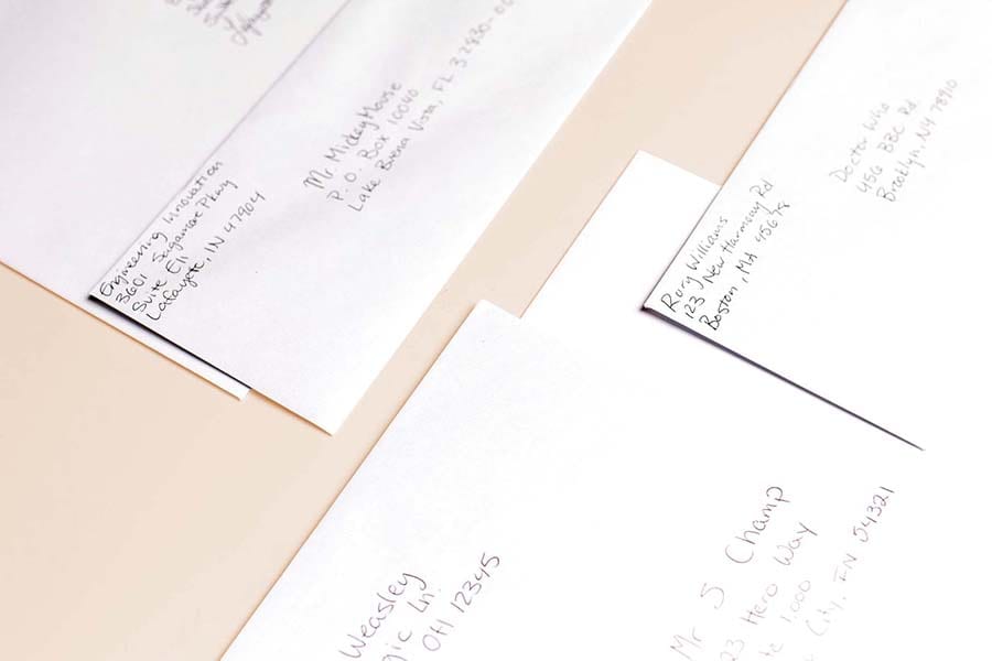 A close-up of several envelopes with handwritten addresses, partially visible on a light surface. The envelopes have names and addresses in different handwriting styles, suggesting they are ready for mailing.